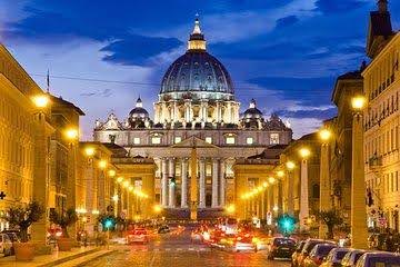 A street with cars driving down it and the dome of st. Peter 's basilica in the background